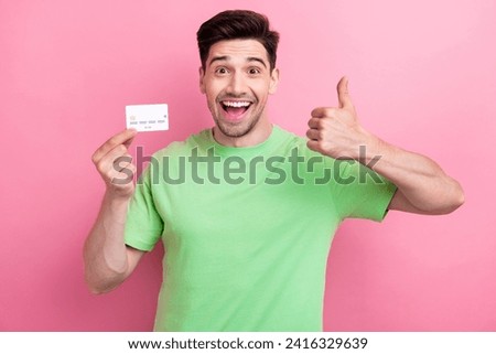 Photo of excited man dressed green t shirt thumb up like sign hold plastic card advertising credit system isolated on pink color background