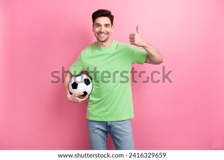 Photo of young amateur cheerful sportsman enjoying betting company holding soccer ball thumb up rate isolated on pink color background
