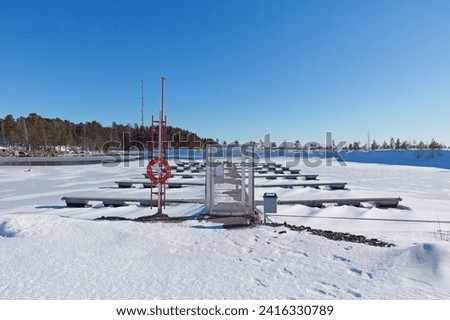 Empty marina with snow covered docks and ground with frozen sea ice on a cold winter day in sunny weather, Loviisa, Finland. Royalty-Free Stock Photo #2416330789