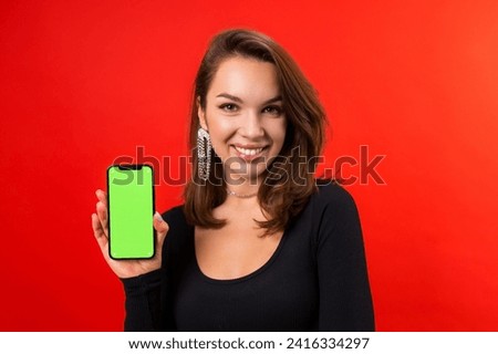 Portrait of a smiling young woman with a mobile phone on a red background. Chromakey on the phone screen, beauty services application