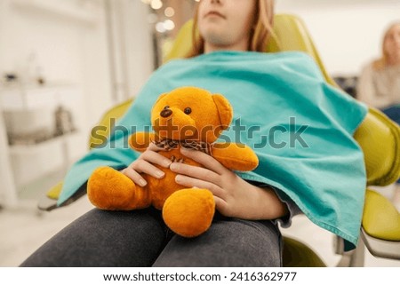 Cropped picture of a young girl holding teddy bear at dentist office.