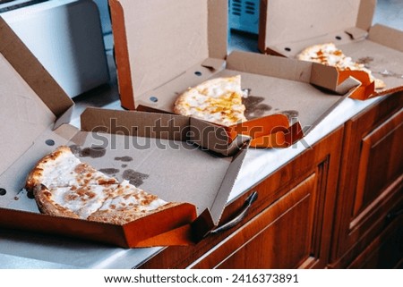 Pieces of pizza in cardboard boxes in the kitchen. Pizza in takeaway paper boxes, ready for delivery. Delivery pizza in a box. Leftover pizza in a delivery box. Royalty-Free Stock Photo #2416373891