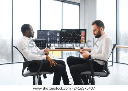 Two smiling confident businessmen, financial analysts or investment advisers sitting at office desk with laptop and documents, business analysis, consulting services, team portrait