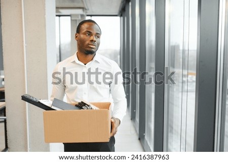 Portrait of african american employee being fired closing laptop with business data while holding tray with personal belongings before leaving. Laid off startup worker cleaning desk before going home. Royalty-Free Stock Photo #2416387963