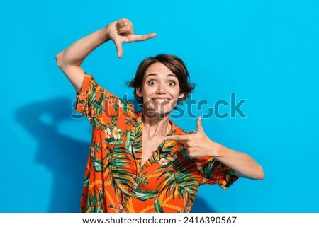 Photo of cheerful positive funky girl dressed stylish clothes showing you two hands making picture isolated on blue color background