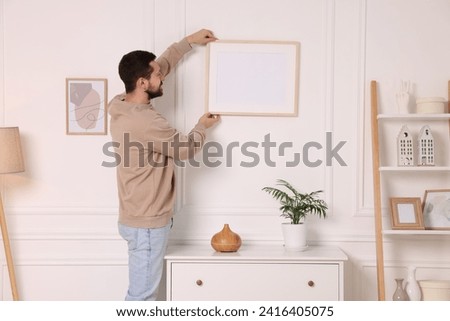 Man hanging picture frame on white wall at home