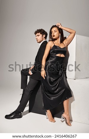romantic and young couple in elegant evening wear posing together near cubes on grey background Royalty-Free Stock Photo #2416406267