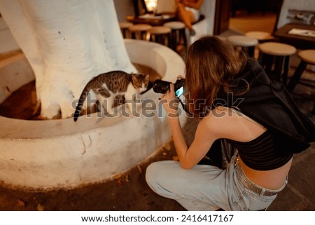 Girl takes a photo of a kitten on the street.
