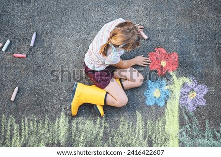 Cute little girl and flowers painted with colorful chalks on asphalt. Happy preschool child having fun with painting chalk picture. Creative leisure for children, drawing and painting.