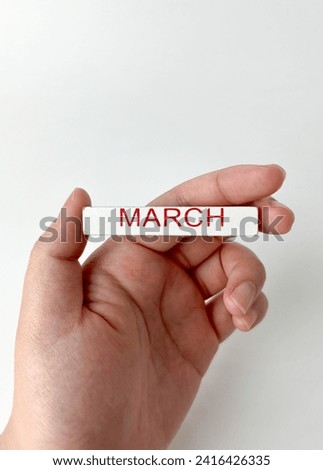 Hand holding wooden block object with march month bulan maret word saying isolated on vertical ratio white background.