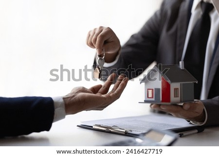 Real estate agent holding house keys is handing them over to a client after signing a home purchase contract agreement.