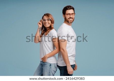 Portrait of attractive smiling man and woman wearing white t shirt and stylish eyeglasses isolated on blue background. Happy confident fashion models posing for pictures in studio 