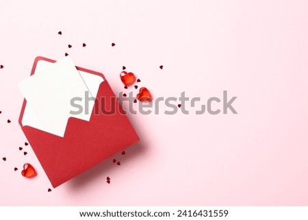 Red paper envelope with blank white note mockup inside, red hearts and confetti on pastel pink background.