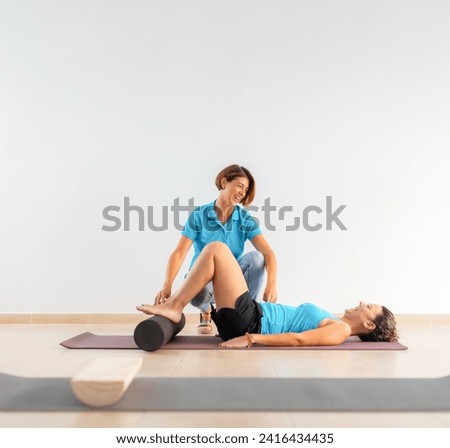 A physiotherapist helps a patient, lying on the floor, during a therapeutic Pilates workout session Royalty-Free Stock Photo #2416434435