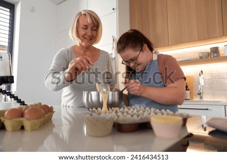 Down syndrome woman and her mother making homemade cupcakes Royalty-Free Stock Photo #2416434513