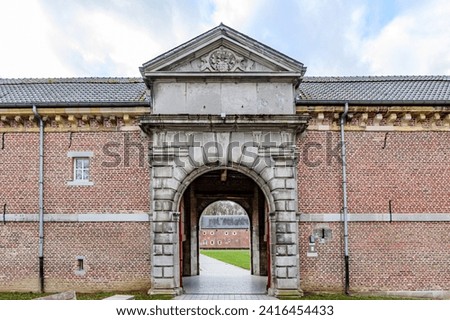 Arched entrance to 16th century Alden Biesen Castle, brick walls and gable roof, courtyard with green grass in background, cloudy day in Bilzen, Limburg, Belgium Royalty-Free Stock Photo #2416454433