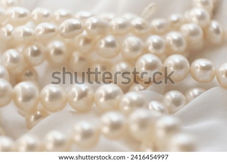 A string of natural pearls lay elegantly on a pale canvas, their soft focus creating a dreamy atmosphere. This image evokes a return to natural beauty amidst the modern era's harsh synthetic Royalty-Free Stock Photo #2416454997