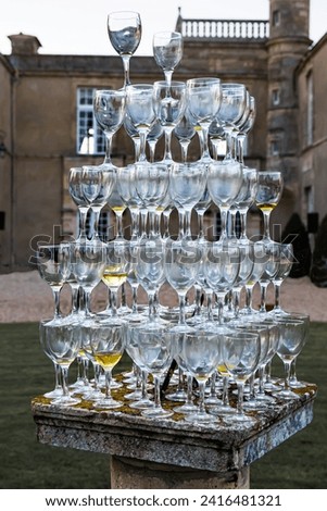 A large number of wine glasses are precariously stacked on a stone pedestal.  This picture was taken at the end of a garden event in France.
