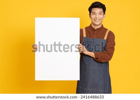Restaurant owner sme young Asian man is holding white blank banner or empty copy space advertisement board isolated on yellow background, Looking at camera