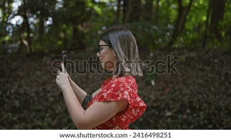 Smiling beautiful hispanic woman with glasses taking stunning picture at meiji temple, immersing in japanese culture using her smartphone technology, indulging in nature at green tokyo park.