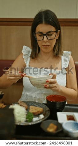 Gorgeous hispanic woman savoring delicacy, eating white rice with chopsticks at chic restaurant