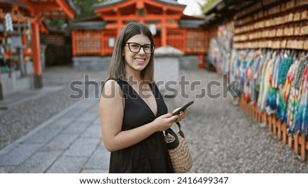 Beautiful young hispanic woman wearing glasses taking pictures to japanese ema wooden boards at fushimi inari-taisha