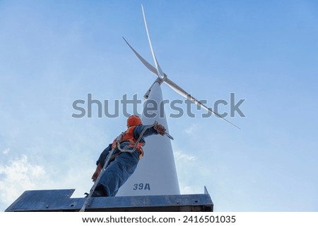 worker in Personal Protective Equipment work with wind turbine farm.  people in Safety Harness work on wind mill. Royalty-Free Stock Photo #2416501035