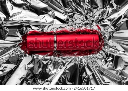 Red elegant lipstick tube pack lying on crumpled silver foil background