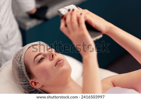 girl lying on a couch in a beauty salon taking a photo of her face after cosmetic procedure