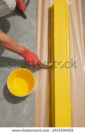 Professional painter at work. Unrecognizable young man uses a paint brush to apply special acrylic paint for road marking on kerbstone.