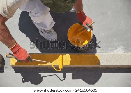 Unrecognizable professional painter at work. Young man uses a paint roller to apply yellow paint for road marking on a parking lot.	