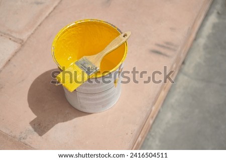 Paint brush on a yellow paint bucket ready to apply special acrylic paint for road marking on asphalt of a parking lot.	