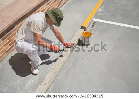 Unrecognizable professional painter at work. Young man uses a scraper to clean a curbstone of a parking lot.