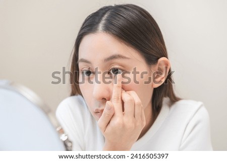 Ophthalmology care, eye sight, vision concept. Asian young woman, female hand holding and putting, wearing soft contact lenses with finger on face, girl looking in mirror at home, beauty and health. Royalty-Free Stock Photo #2416505397