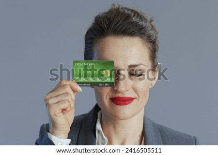 relaxed trendy female worker in gray suit with credit card isolated on grey.