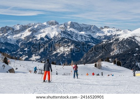Ski resort in the Dolomites. Alpine skiers ski on the ski slopes. Ski slopes in the Dolomites. Alpine skiing sport and recreation. Group of people skiing and snowboarding down the slope.