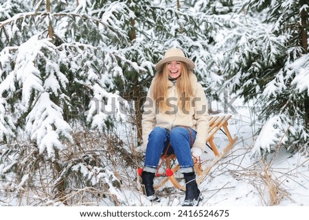 Girl sledding in winter forest. Young blonde woman has fun in snowy woods and laughs. 