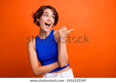 Photo of pretty excited lady wear blue singlet pointing thumb looking empty space isolated orange color background