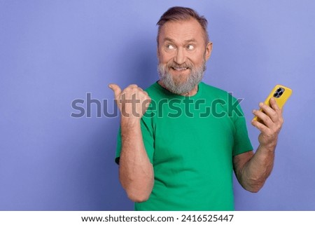 Portrait of cheerful grandfather hold smart phone look indicate finger empty space isolated on purple color background