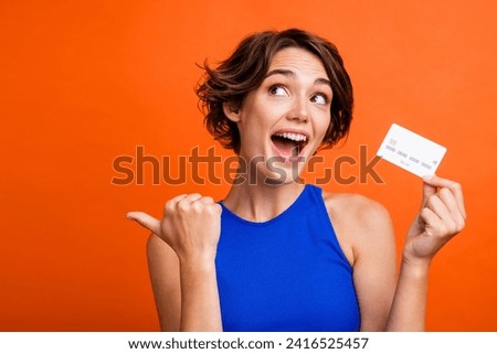 Portrait of cute impressed person arm hold plastic debit card look indicate finger empty space isolated on orange color background