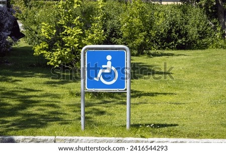Wheelchair handicap sign in a parking against the backdrop of a green lawn. 