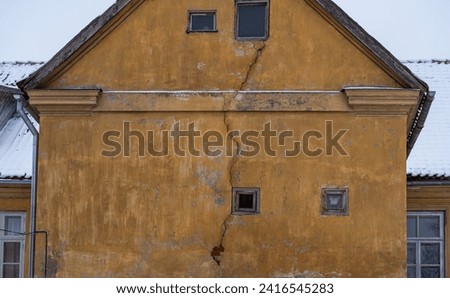 Damaged yellow house with crack in the wall, old building facade part of.