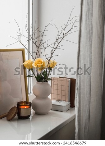 Cozy composition still life on the window - a bouquet of yellow roses,  books, a burning candle - a cozy home concept