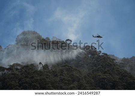 BOGOTA,BOGOTA DC, COLOMBIA - 01232024 Helicopter carrying giant bucket of water to extinguish a fire in the mountain Royalty-Free Stock Photo #2416549287