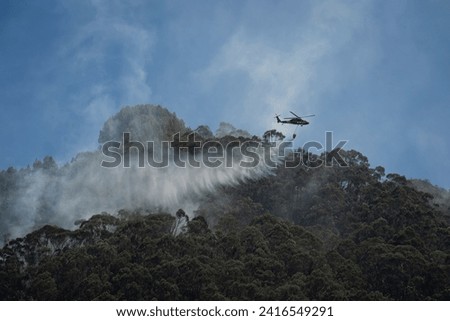 BOGOTA,BOGOTA DC, COLOMBIA - 01232024 Helicopter carrying giant bucket of water to extinguish a fire in the mountain Royalty-Free Stock Photo #2416549291
