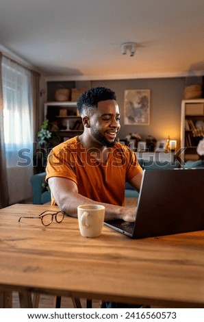 Young African American man sitting at home using laptop for video call. Royalty-Free Stock Photo #2416560573
