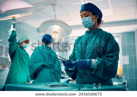 Female surgical technician assisting during the surgery in operating room. Royalty-Free Stock Photo #2416560673