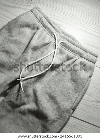 Elastic band on the waist of sports joggers close up. Warm fleece fabric light gray tracksuit high waisted pants with pockets and white drawstring. White gray wooden texture background 