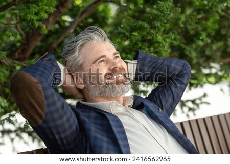 A 45 year old caucasian male in a dark blue blazer and white t-shirt, relaxing outdoors with a contented smile, exuding a serene and happy mood.
