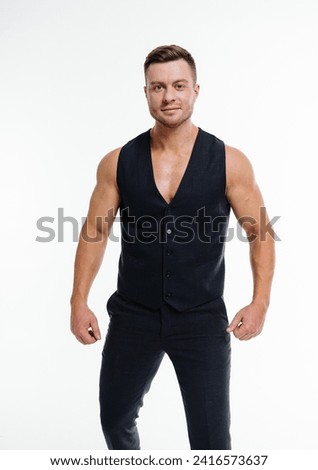 Man in Black Vest Poses for Picture Against a Neutral Background. A stylish man wearing a black vest strikes a pose against a plain backdrop, ready for a photoshoot.